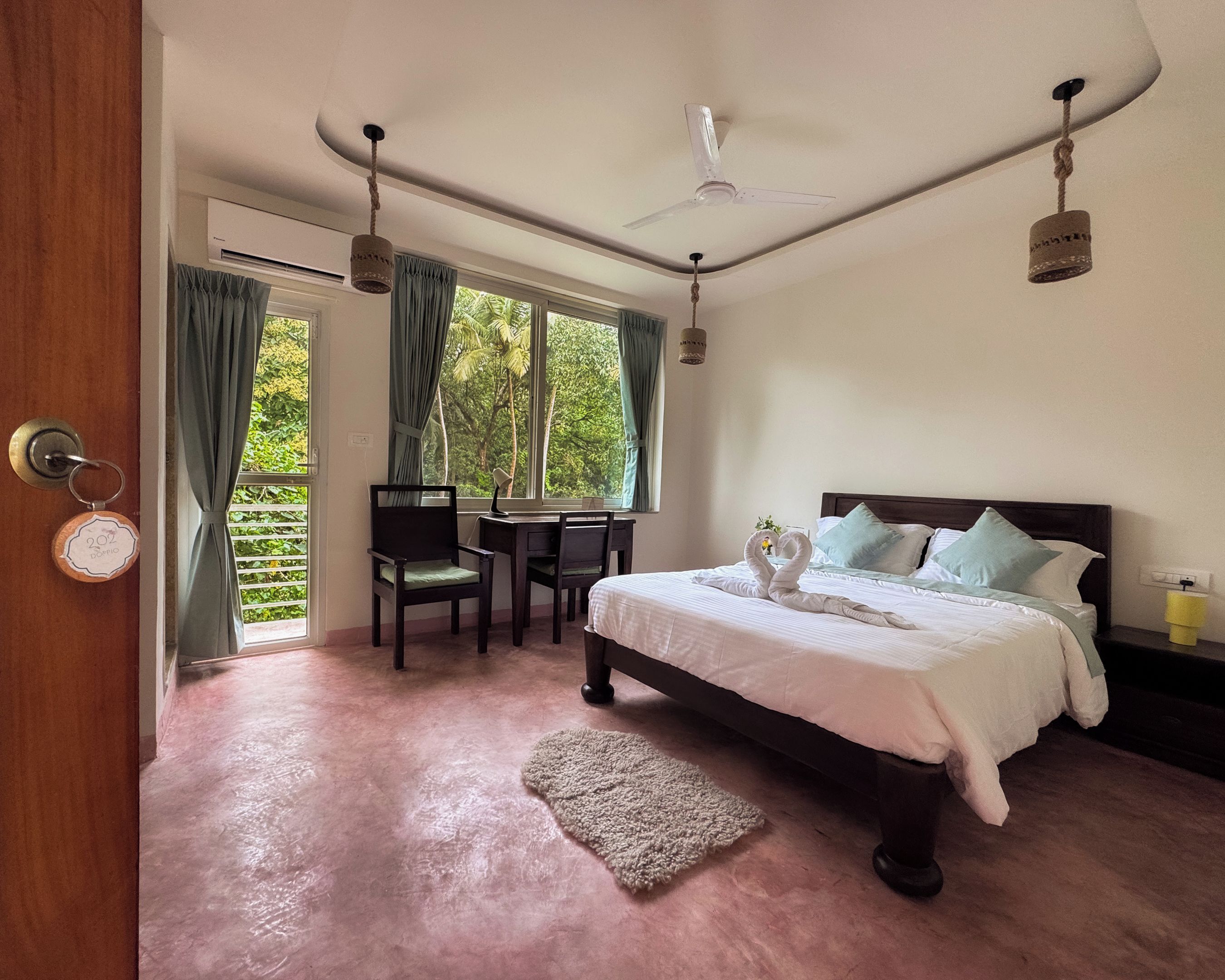 A bedroom with a bed, a desk, and a chair. There is a window with curtains, a ceiling fan, and a rug on the floor.