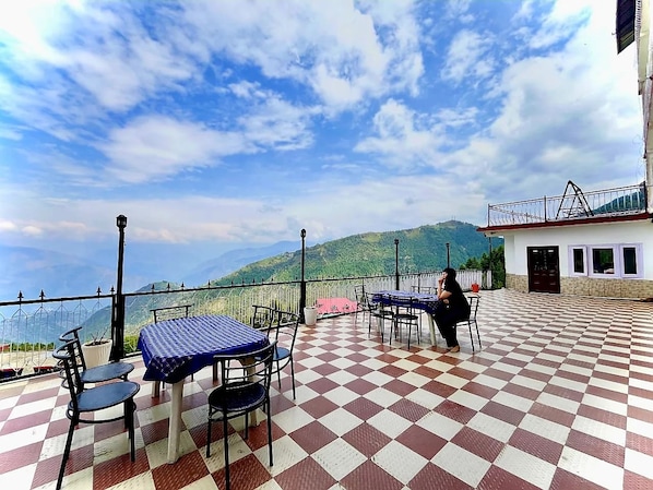 Una terraza al aire libre con piso a cuadros, mesas con manteles azules y sillas.
