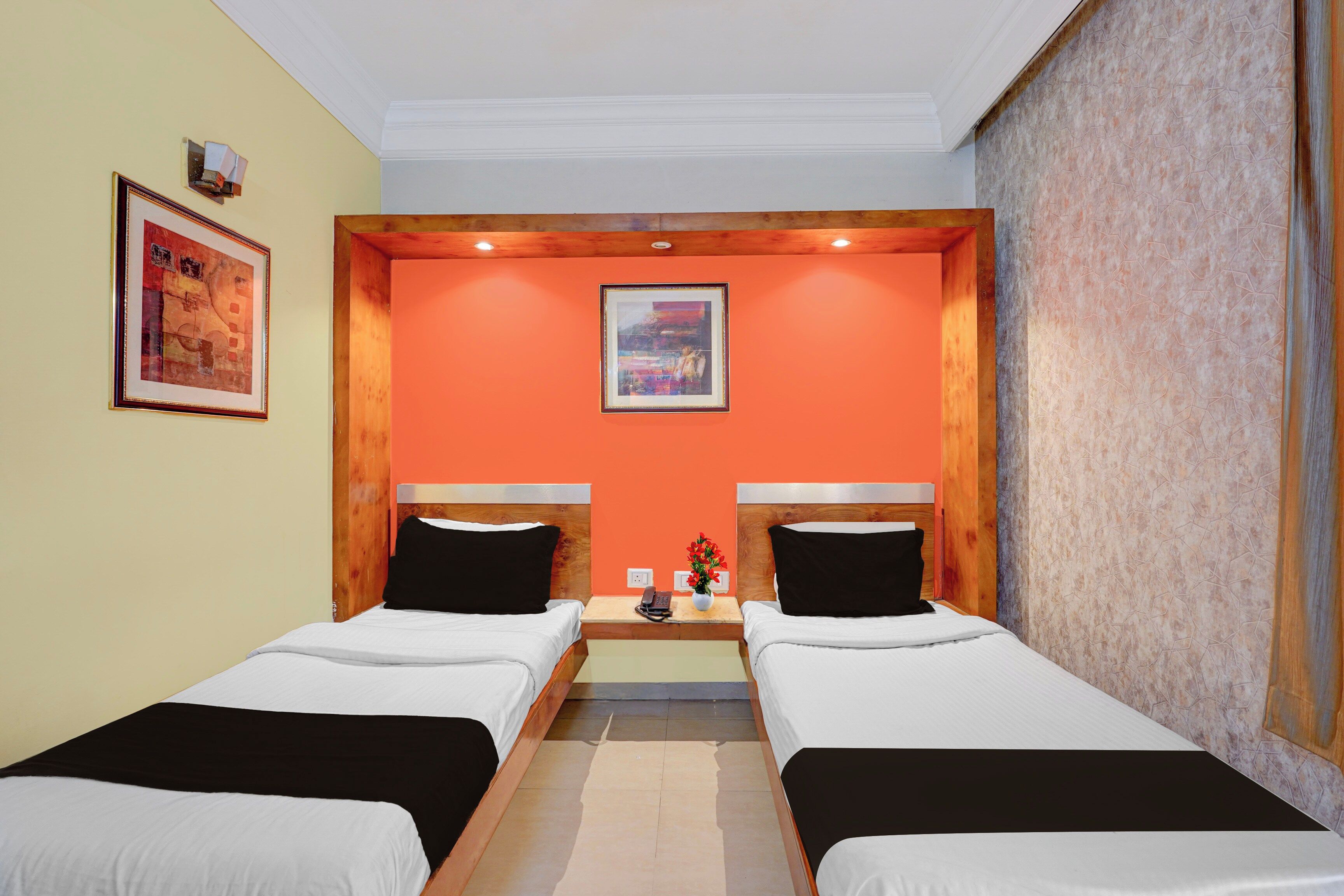 Una habitación de hotel con dos camas, un cuadro en la pared y una mesita con un jarrón de flores.