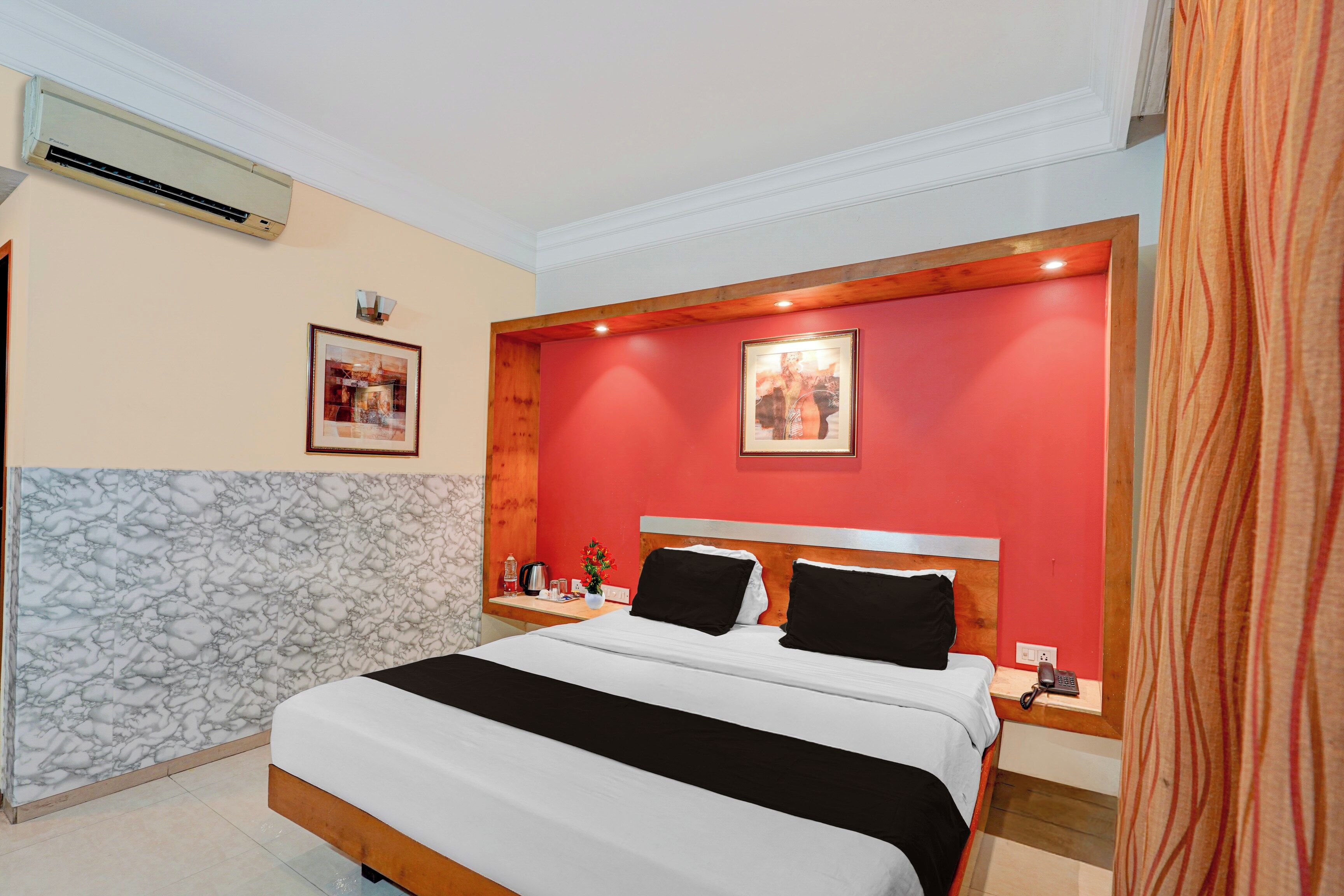 Habitación de hotel con una cama, una mesita de noche, aire acondicionado de pared y dos cuadros enmarcados.
