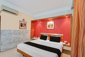 Habitación de hotel con una cama, una mesita de noche, aire acondicionado de pared y dos cuadros enmarcados.