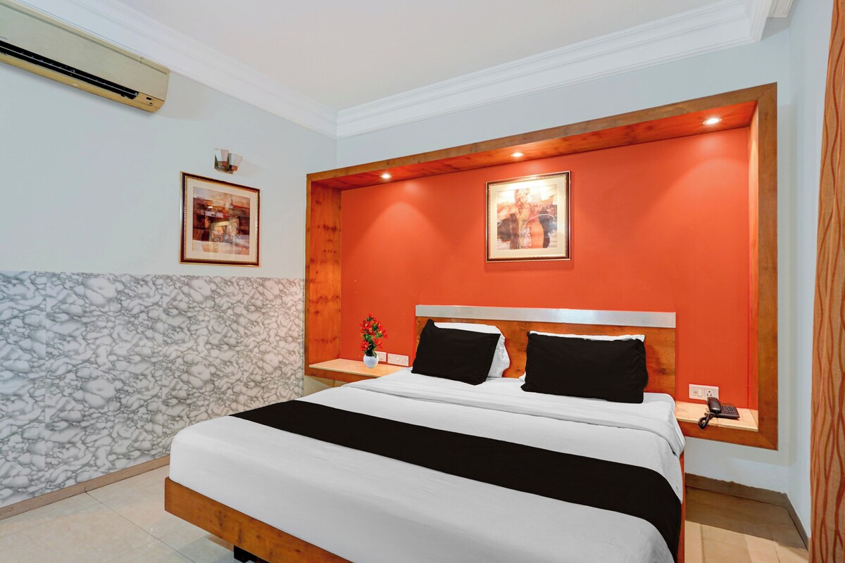 A hotel room with a bed, a nightstand, a wall-mounted phone, and two framed pictures.
