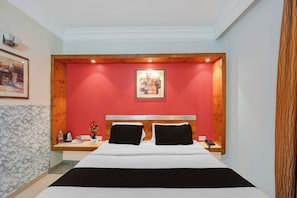 Habitación de hotel con cama, mesita de noche, un cuadro y una pared de acento roja.