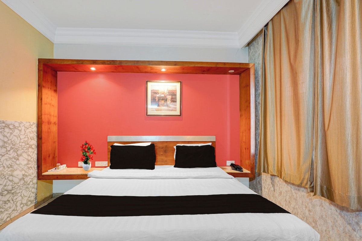 Una habitación de hotel con cama, mesita de noche, teléfono, un cuadro en la pared y un florero con flores.