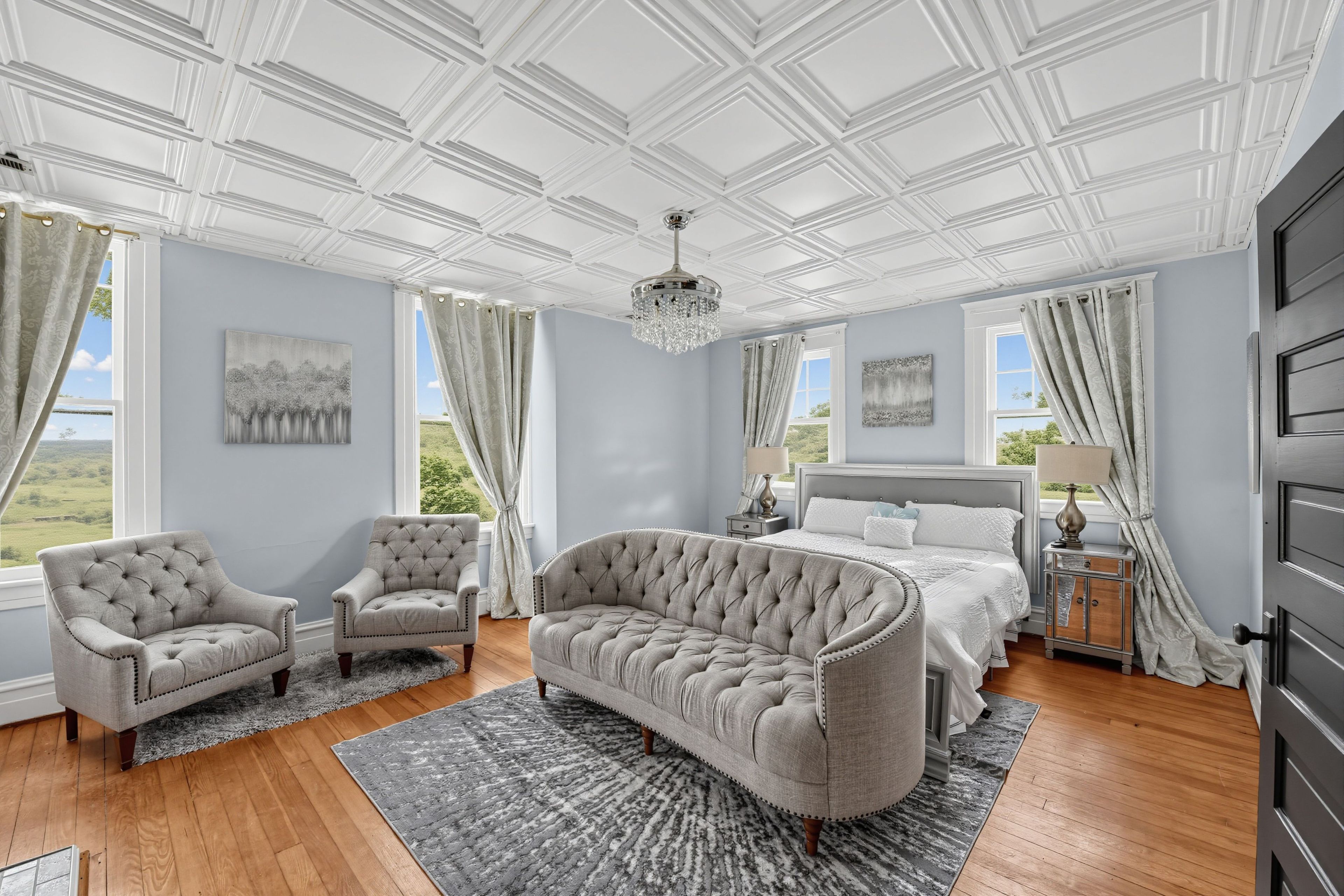 A spacious bedroom with a large bed, two armchairs, a chaise lounge, and a chandelier.