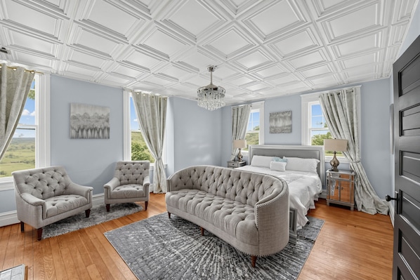 A spacious bedroom with a large bed, two armchairs, a chaise lounge, and a chandelier.
