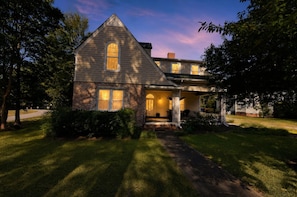 A two-story house with a brick facade, a gabled roof, and a front porch with a bench.