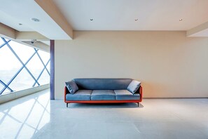 Ein modernes Interieur mit einem einzelnen blauen Ledersofa vor einer schlichten Wand, großen Fenstern und einem geometrischen Deckenmuster.