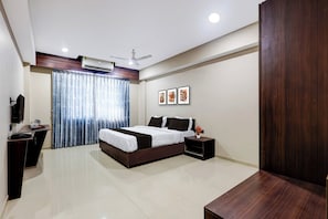 A modern hotel room with a bed, bedside table, and a desk with a chair.