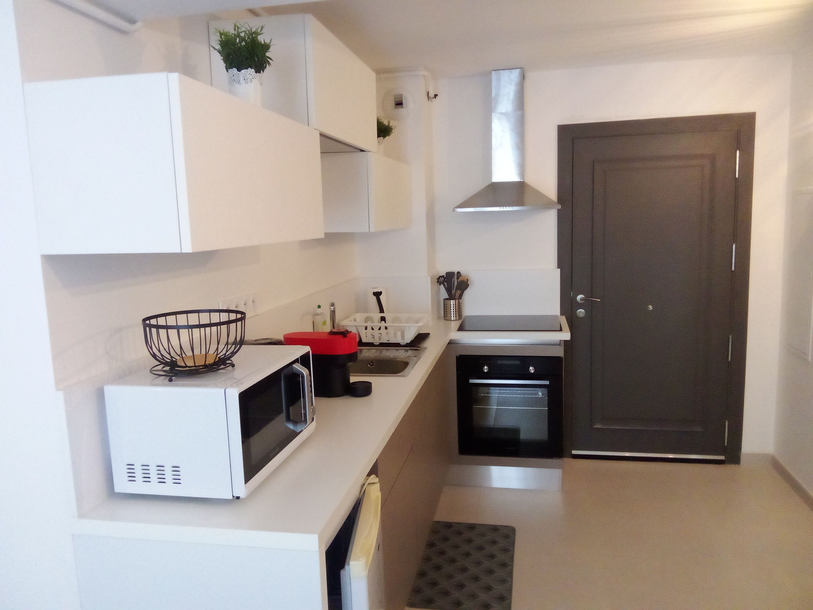 Una cocina compacta con muebles blancos, un microondas, una estufa y una puerta.