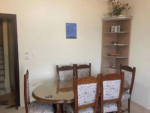 A dining area with a round table and floral upholstered chairs, a small blue painting on the wall, and a wooden cabinet with shelves. - Apartment With Side Sea Views ,near El Gouna (Hurghada)