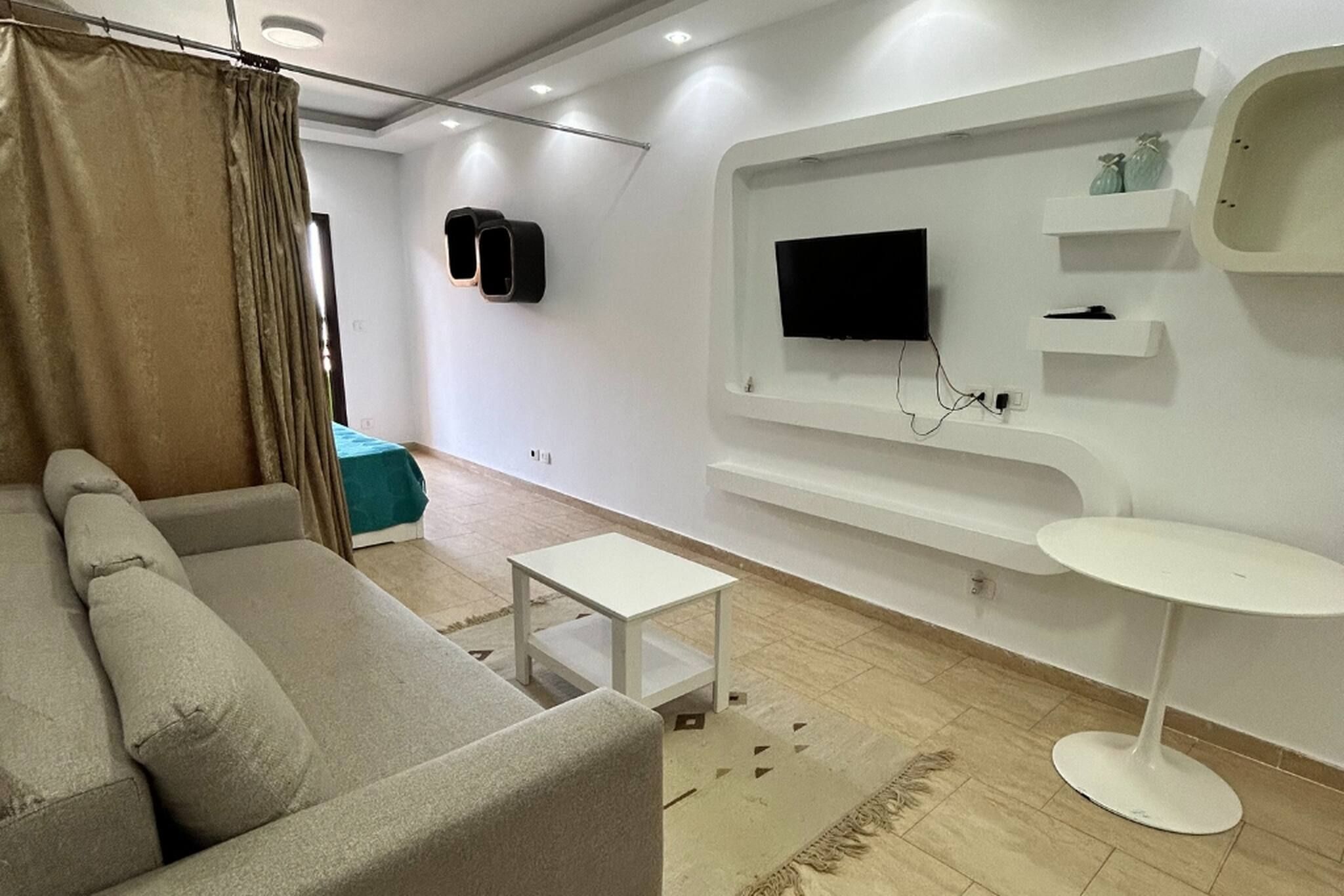 A modern living room with a sofa, a small table, a TV mounted on the wall, and a white side table.