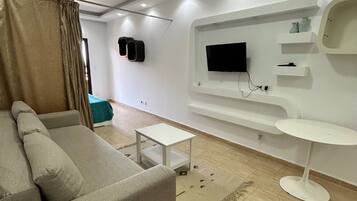 A modern living room with a sofa, a small table, a TV mounted on the wall, and a white side table.