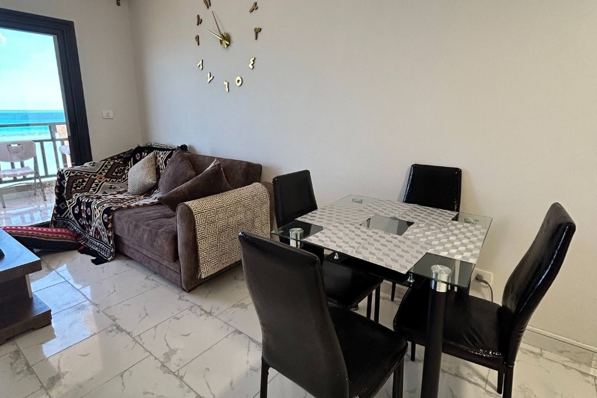 A living area with a sofa, a dining table with chairs, and a decorative wall clock.