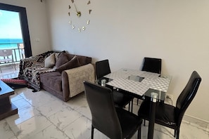 A living area with a sofa, a dining table with chairs, and a decorative wall clock. - 1BR Chalet With Pool, Front Sea View & Balcony (Hurghada)