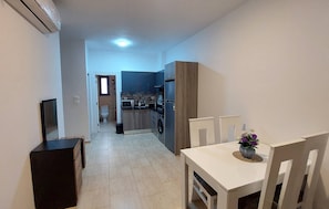 A narrow hallway leading to a kitchen with a microwave, refrigerator, and washing machine. There is a dining area with a table and chairs, and a small window with a view. - Luxurious Chalet in Red Sea Governorate With Stunning Sea Views (Hurghada)