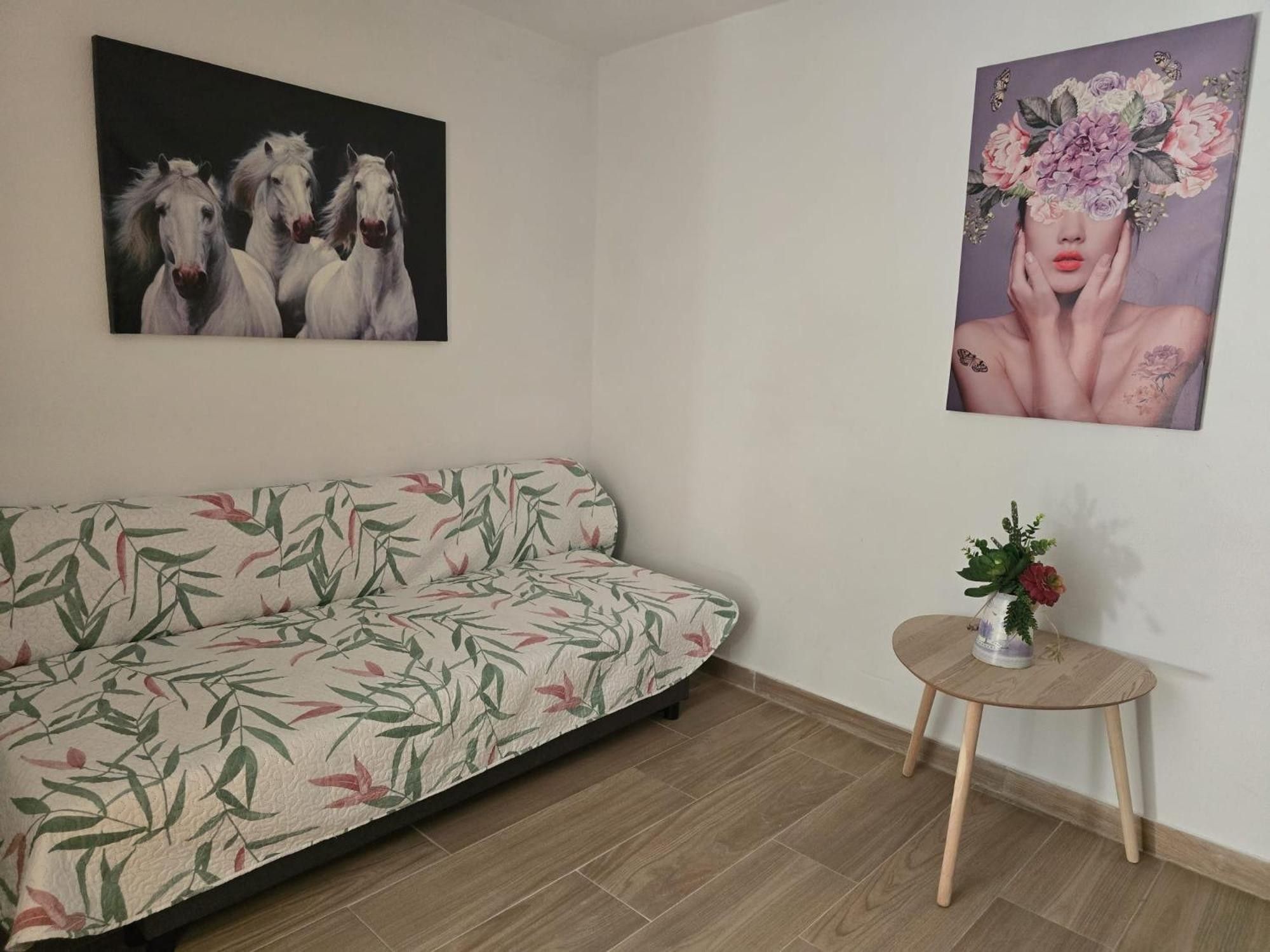 A room with a sofa, a small round table with a vase, and two wall-mounted artworks.