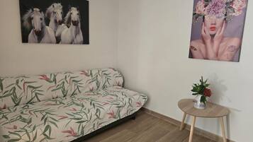 A room with a sofa, a small round table with a vase, and two wall-mounted artworks.