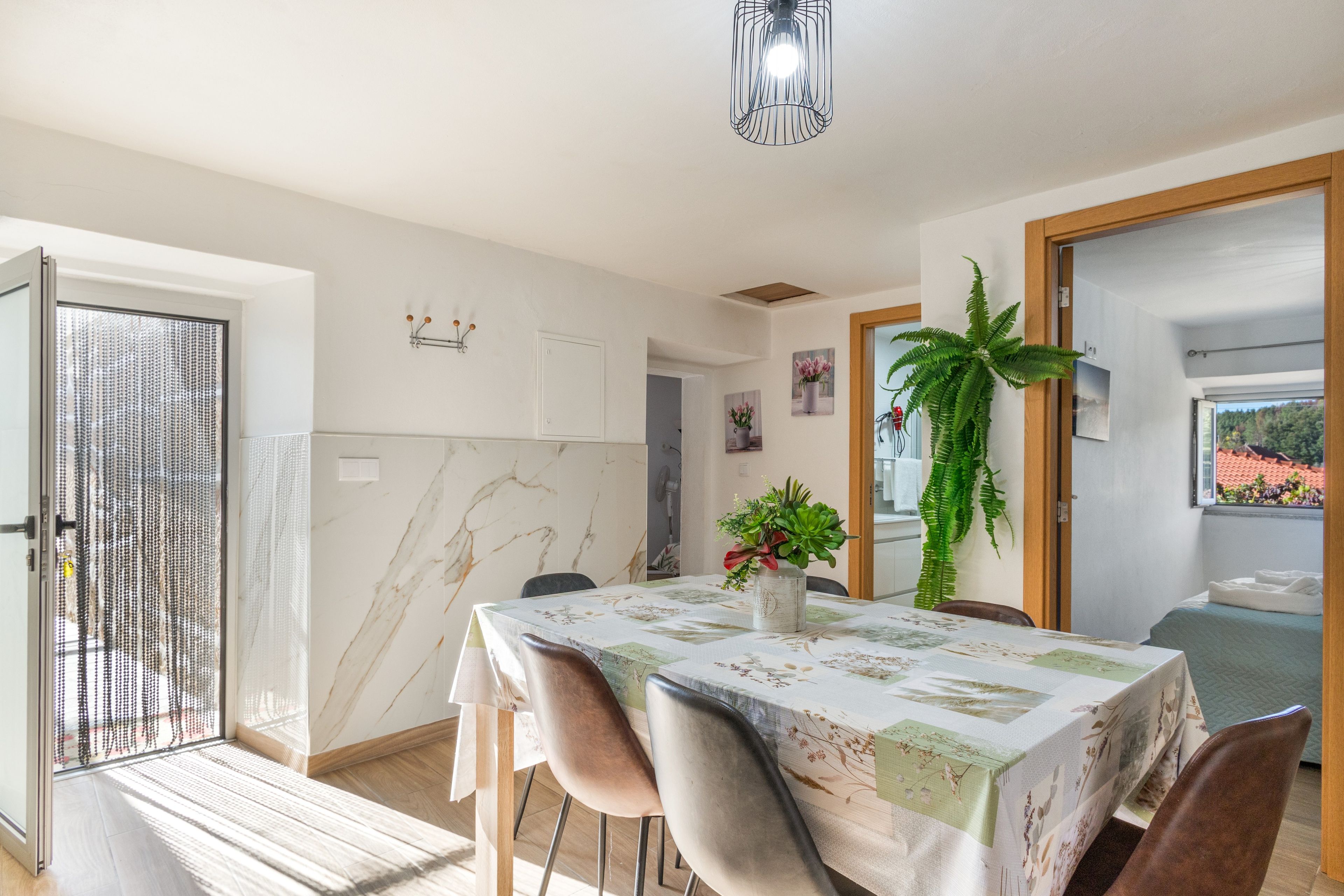 Un coin repas avec une table dressée pour deux personnes, une plante en pot et une vue sur un balcon.