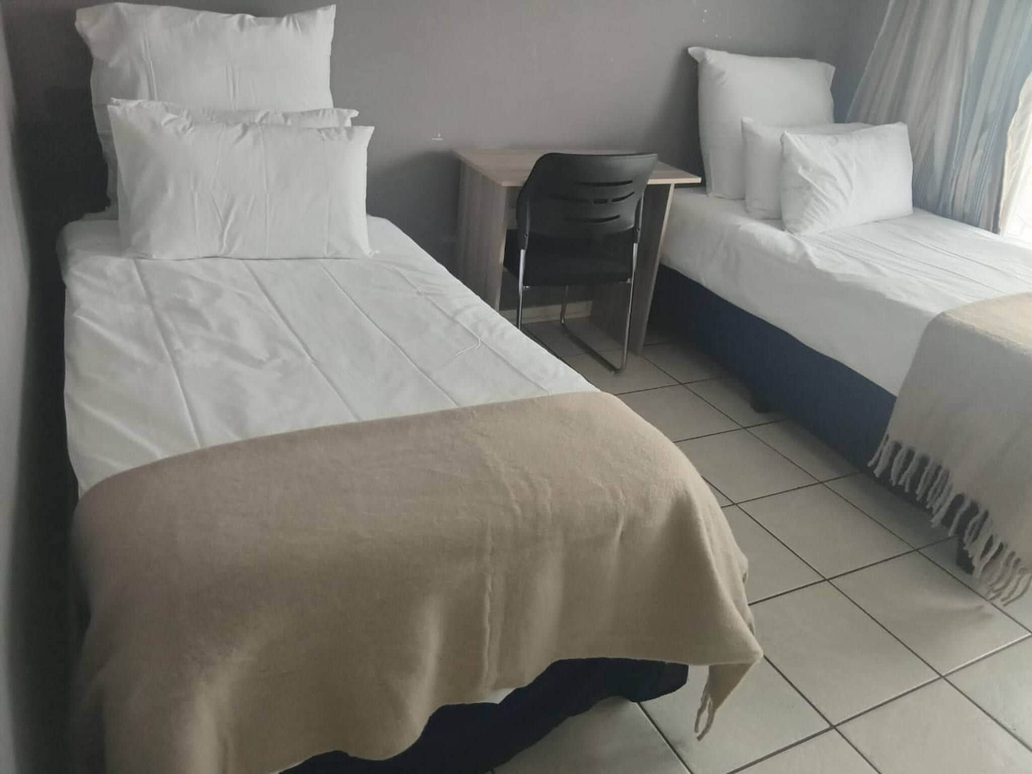A hotel room with two beds, a desk, and a chair.
