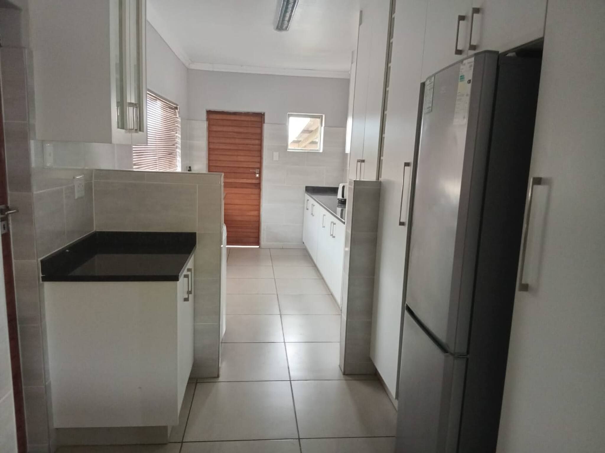 Una cocina con armarios blancos, un refrigerador de acero inoxidable y una encimera negra.
