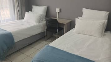 Una habitación de hotel con dos camas individuales, un escritorio, una silla y una ventana con cortinas.