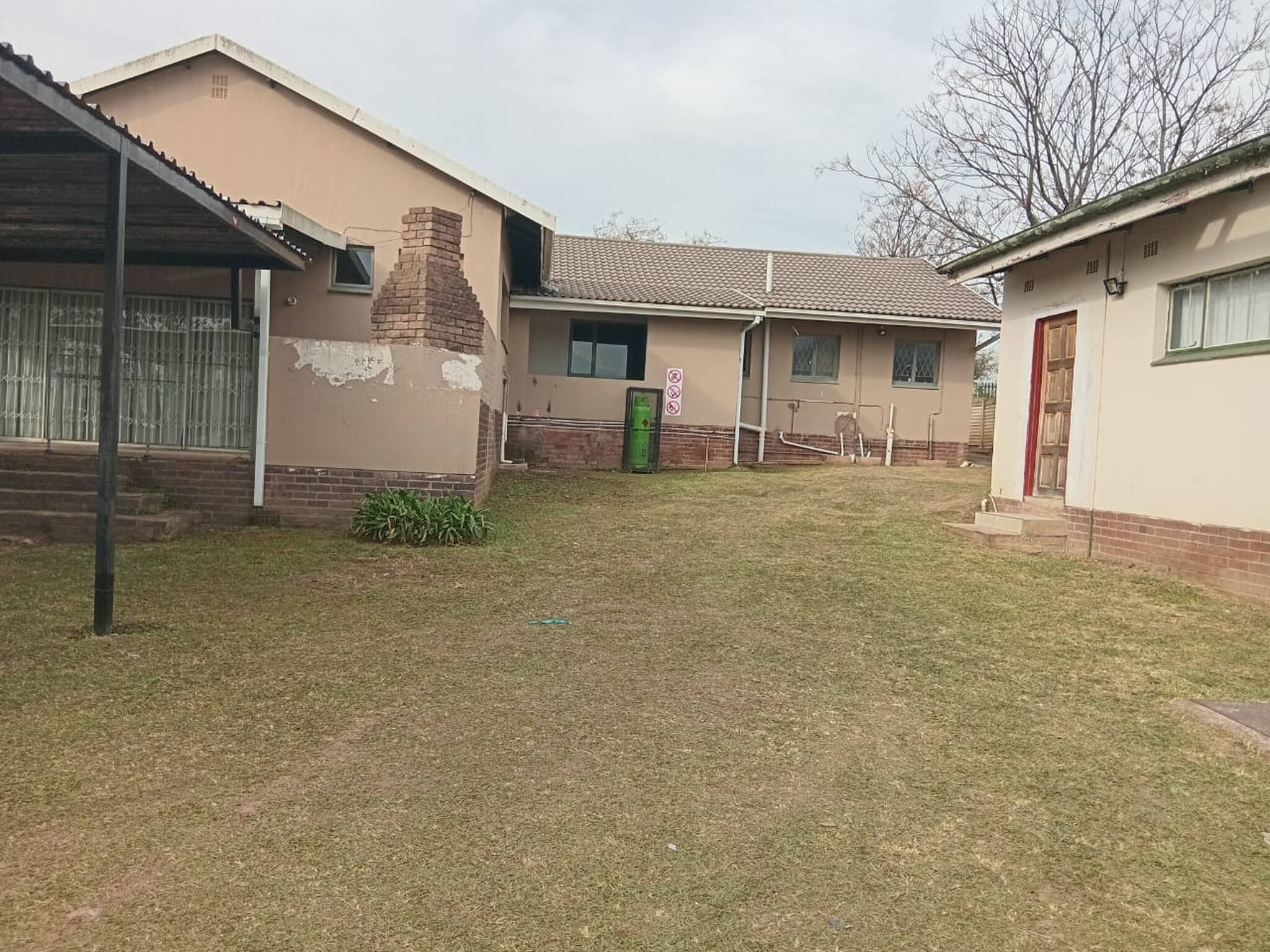 Una propiedad residencial con jardín cercado, una chimenea de ladrillo y un bote de basura verde pequeño.