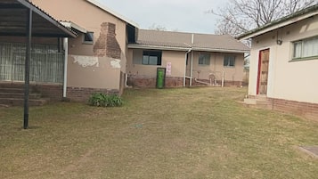 Una propiedad residencial con jardín cercado, una chimenea de ladrillo y un bote de basura verde pequeño.