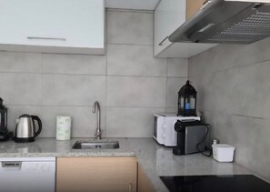 Et moderne køkken med en stålvask, elkedel, brødrister og en sort lanterne på bordpladen.