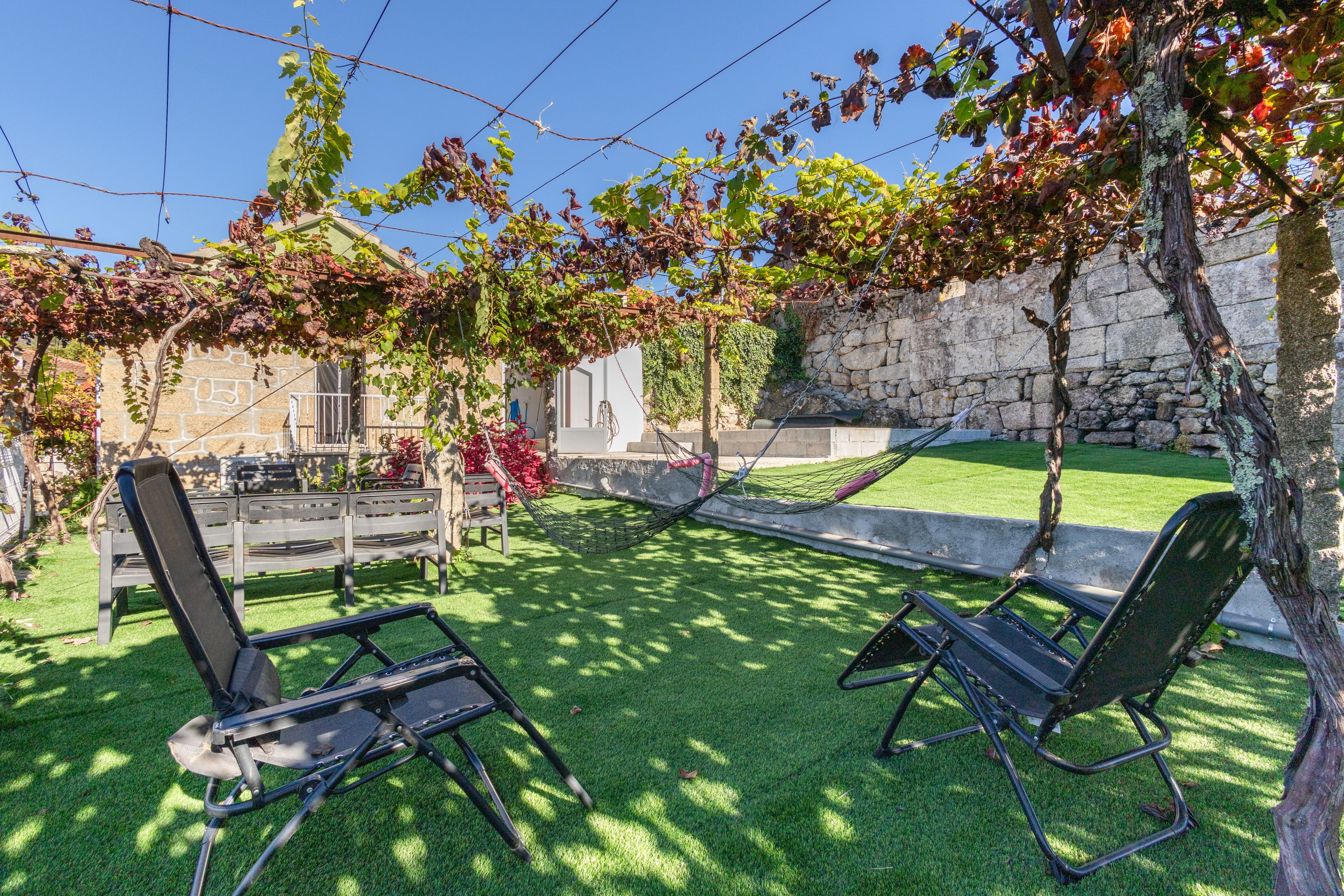 Un patio con due sedie nere, un'amaca e un muro in pietra sullo sfondo.