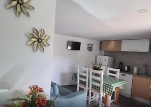 En kompakt opholdsstue med tekøkken, spiseplads med bord og stole samt en sofa.