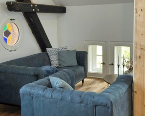 Een kamer met een grote grijze modulaire bank, een ronde salontafel en een deur naar buiten.