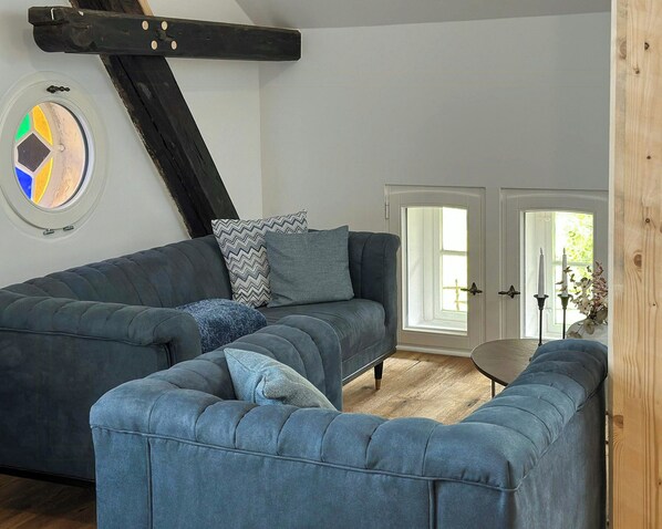 Ein Zimmer mit einem großen, grauen Ecksofa, einem runden Couchtisch und einer zur Außenseite führenden Tür.