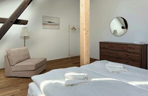 A bedroom with a bed, a wooden dresser, a chair, a hanging light, a mirror, and a painting on the wall. - Historic apartment near the North Sea (Butjadingen)