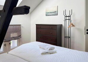 Een slaapkamer met een bed, een dressoir, een schilderij en een kapstok.