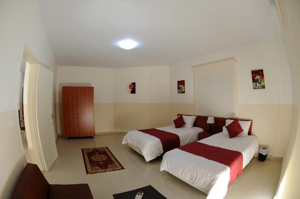 Quarto de hotel com duas camas, um guarda-roupa, um tapete pequeno e uma lixeira.