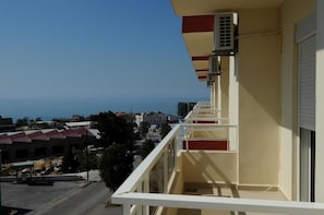 A balcony with a view of the sea, a building with a red and white facade, and a clear sky.