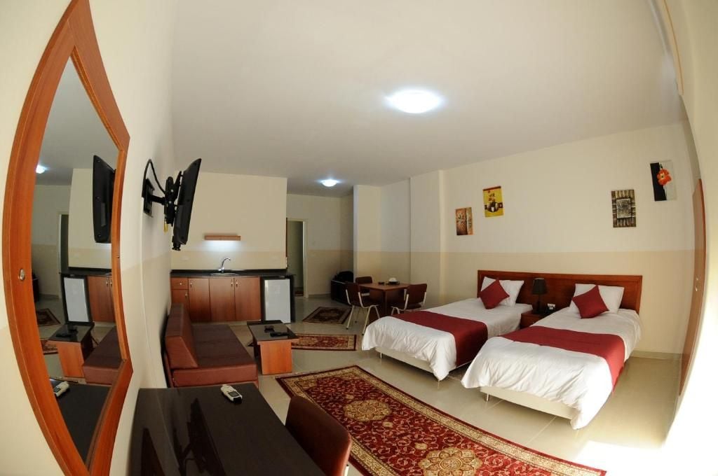 A hotel room with two beds, a desk, a chair, a TV, and a mirror.