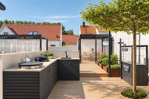 An outdoor kitchen area with a sink, grill, and wooden deck. - New Listing (Skanör)