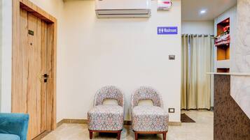 Et receptionsområde med en trädør, en aircondition, skilt til toilettet, to mønstrede stole og en blå sofa.