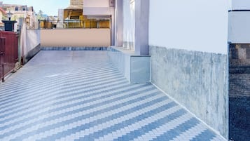 Un étroit couloir extérieur, doté d’un sol carrelé à motifs et d’un mur en béton d’un côté.