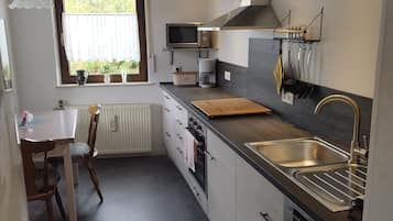 Ett modernt kök med en inbyggd ugn, en mikrovågsugn och en diskho. Det finns ett fönster med utsikt över grönområden utanför.