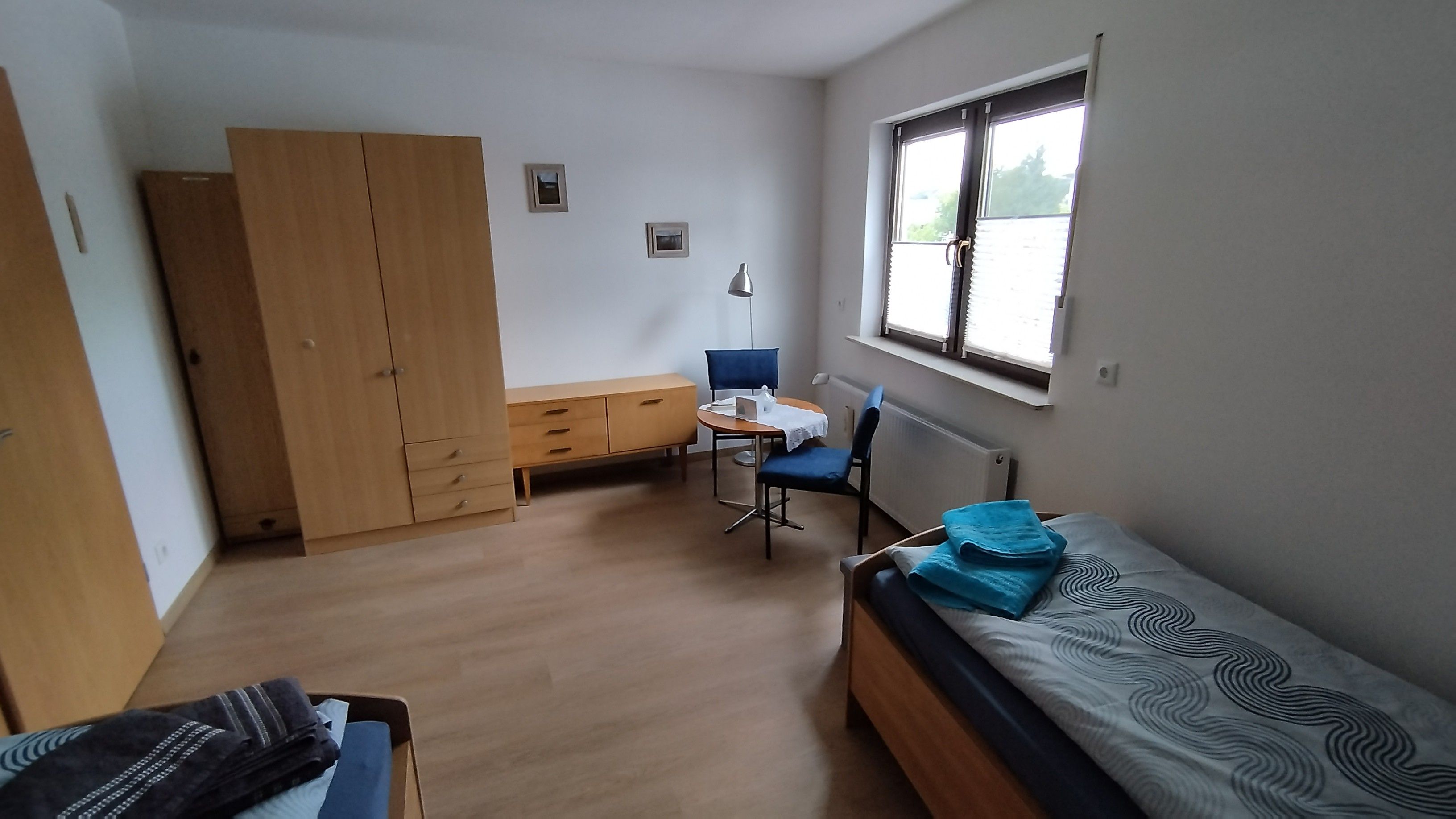 A room with a bed, a desk, a chair, a wardrobe, and a window.