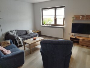 Un salon avec un canapé, une table basse, un téléviseur et une fenêtre avec des rideaux.