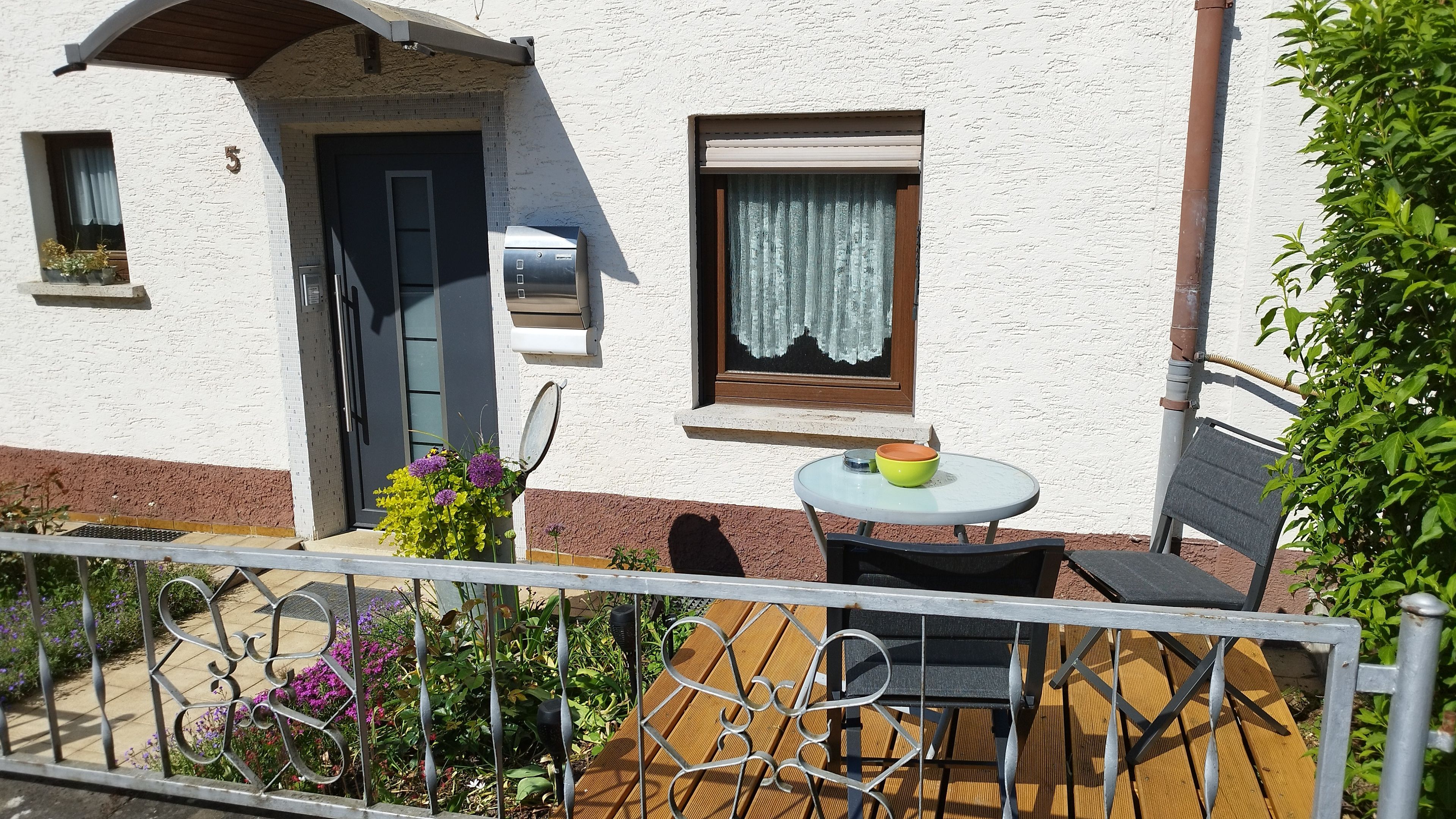 Ein Gebäude mit einer Tür, einem Fenster mit Vorhang und einem kleinen Tisch mit einer Schüssel.