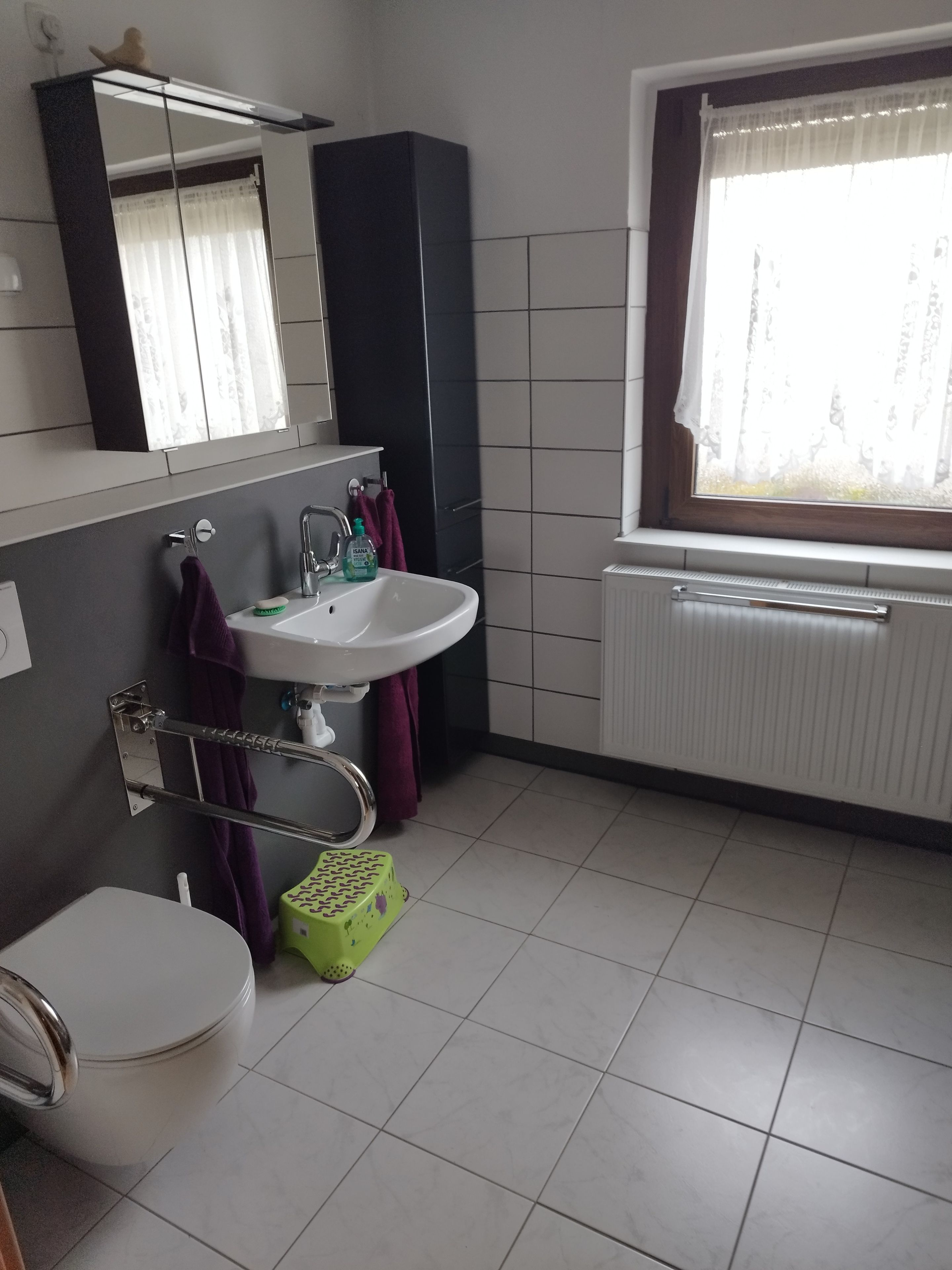 Une salle de bain comprenant des toilettes, un lavabo, un miroir, une fenêtre et un radiateur.