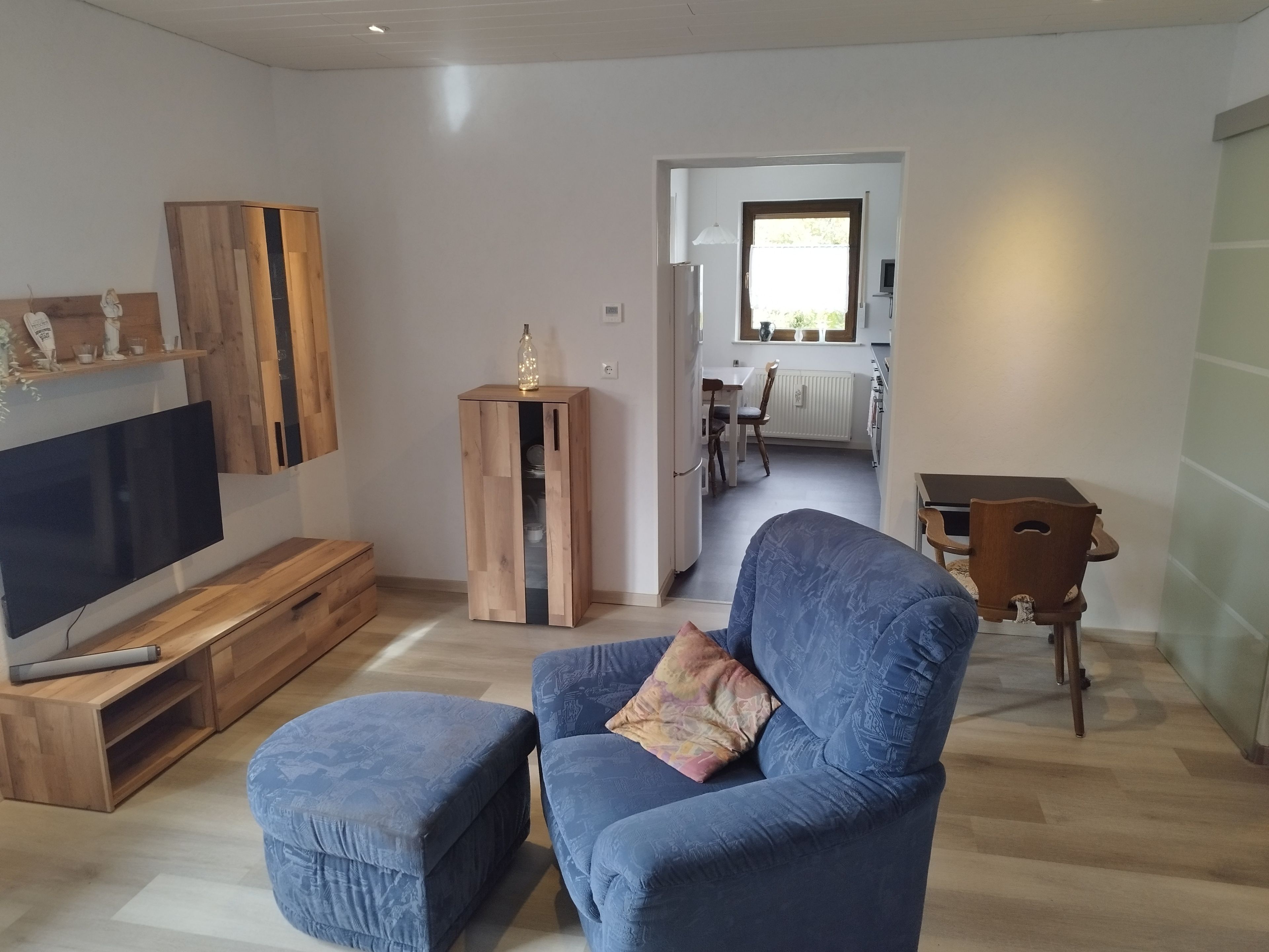A living room with a flat-screen TV, a blue sofa, and a wooden cabinet.