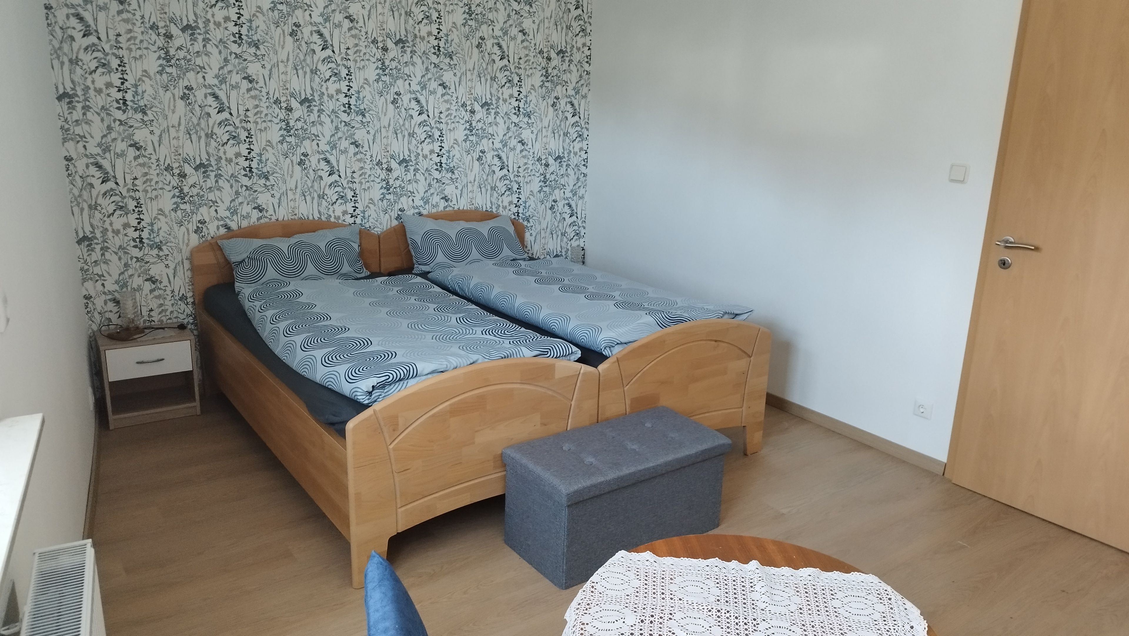 Ein Schlafzimmer mit einem hölzernen Bett, einem Nachttisch, einer kleinen Bank und einer Tür.