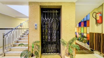 Entrada de un hotel con una reja metálica, una escalera con barandillas de metal y plantas en macetas.