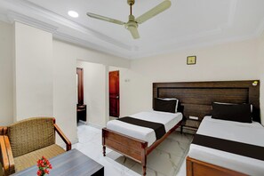 A hotel room with two beds, a wooden headboard, a ceiling fan, a clock, and a small table with a vase of flowers. - Townhouse Godavarikhani Bus Terminal (Karimnagar)